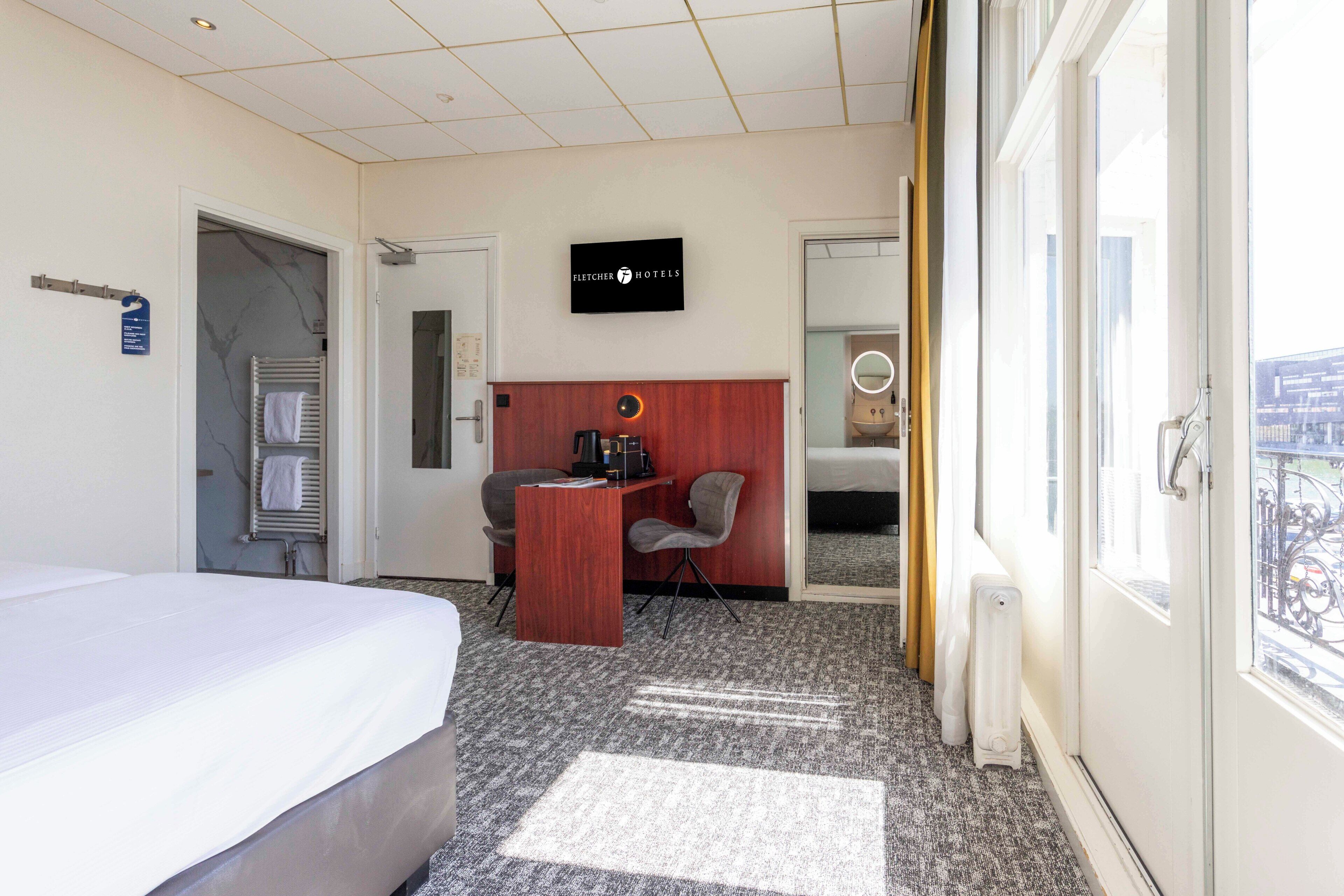 Ein Hotelzimmer mit Bett, Schreibtisch, Stuhl, Heizkörper und Fenster mit Blick.