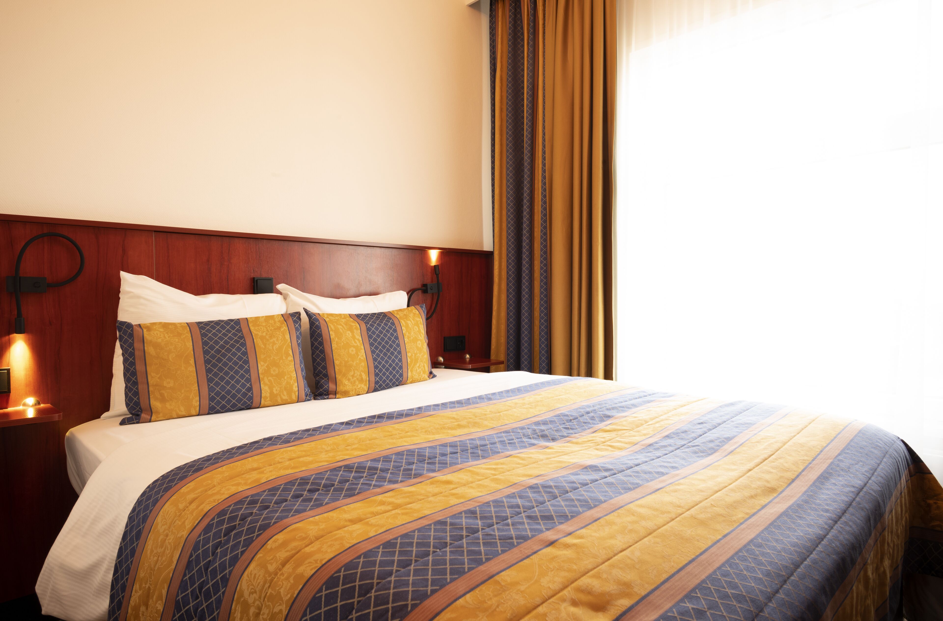 A hotel room with a large bed, wooden headboard, and a nightstand with a lamp.