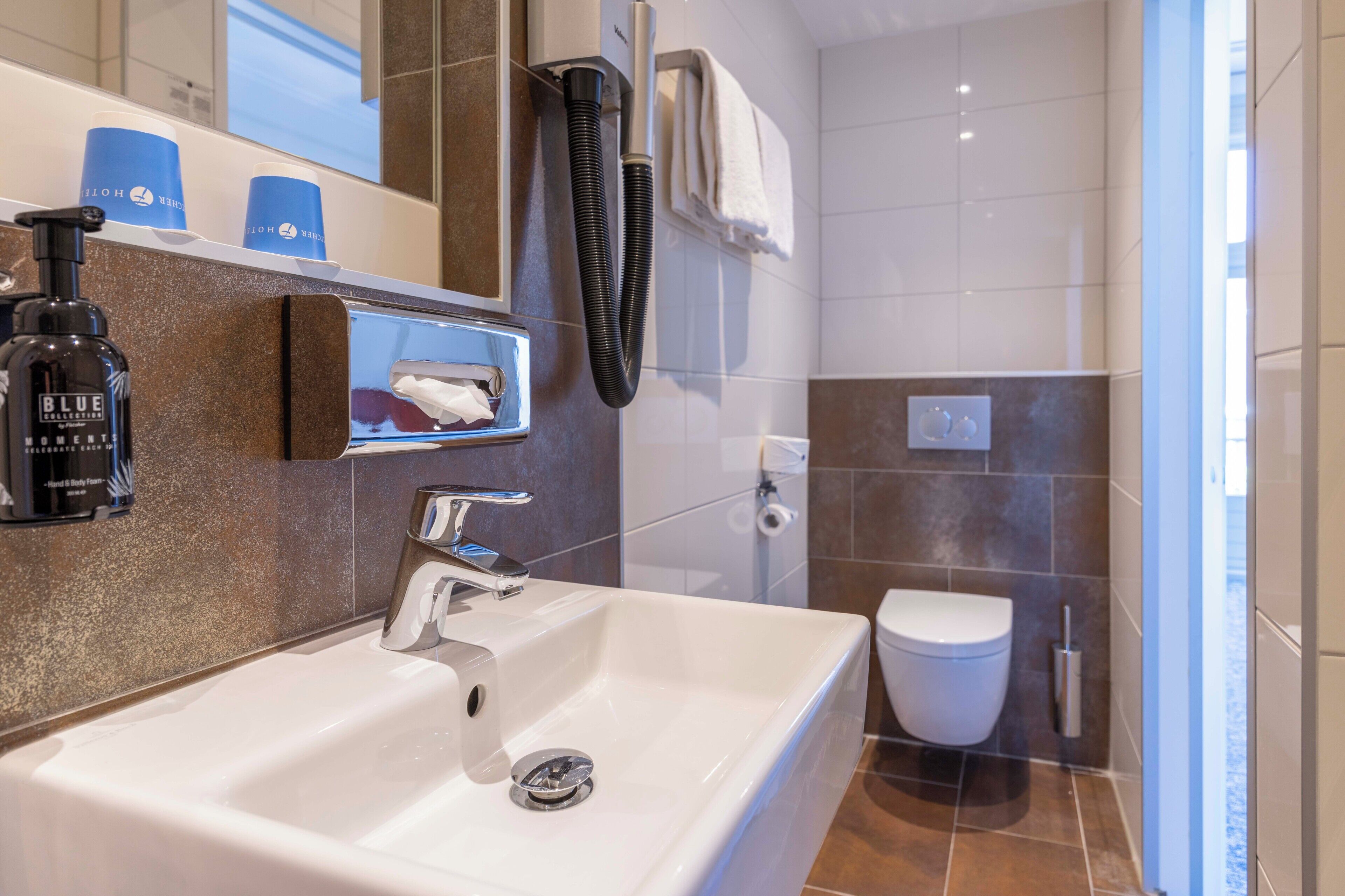 Un baño moderno con un lavamanos blanco, un cabezal de ducha de mano, un inodoro y un perchero para toallas.