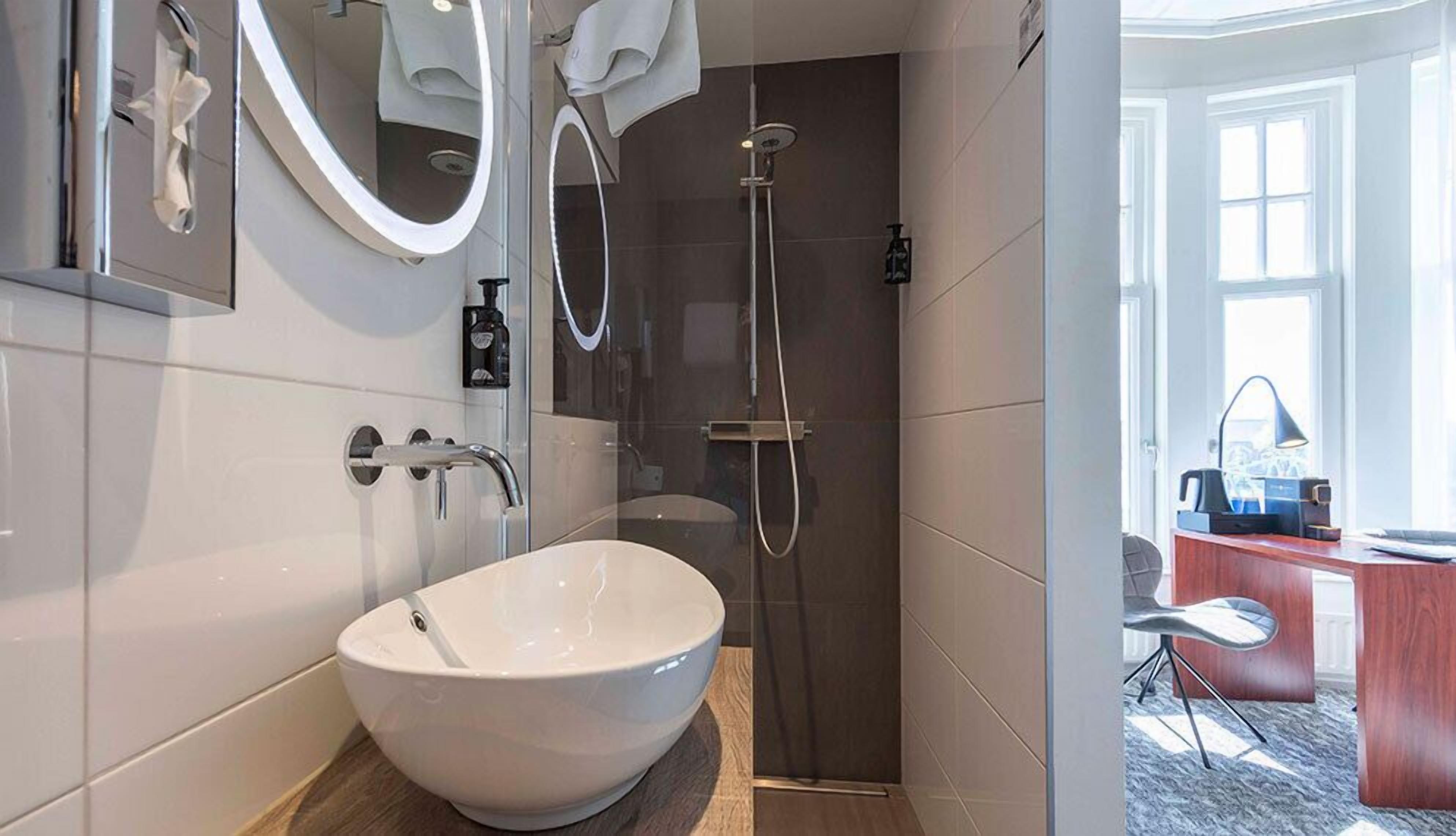A modern bathroom with a large white sink, a glass-enclosed shower, and a mirror above the sink.
