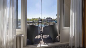 Habitación con un ventanal grande que da a una masa de agua, muebles de mimbre y vista a un puente.