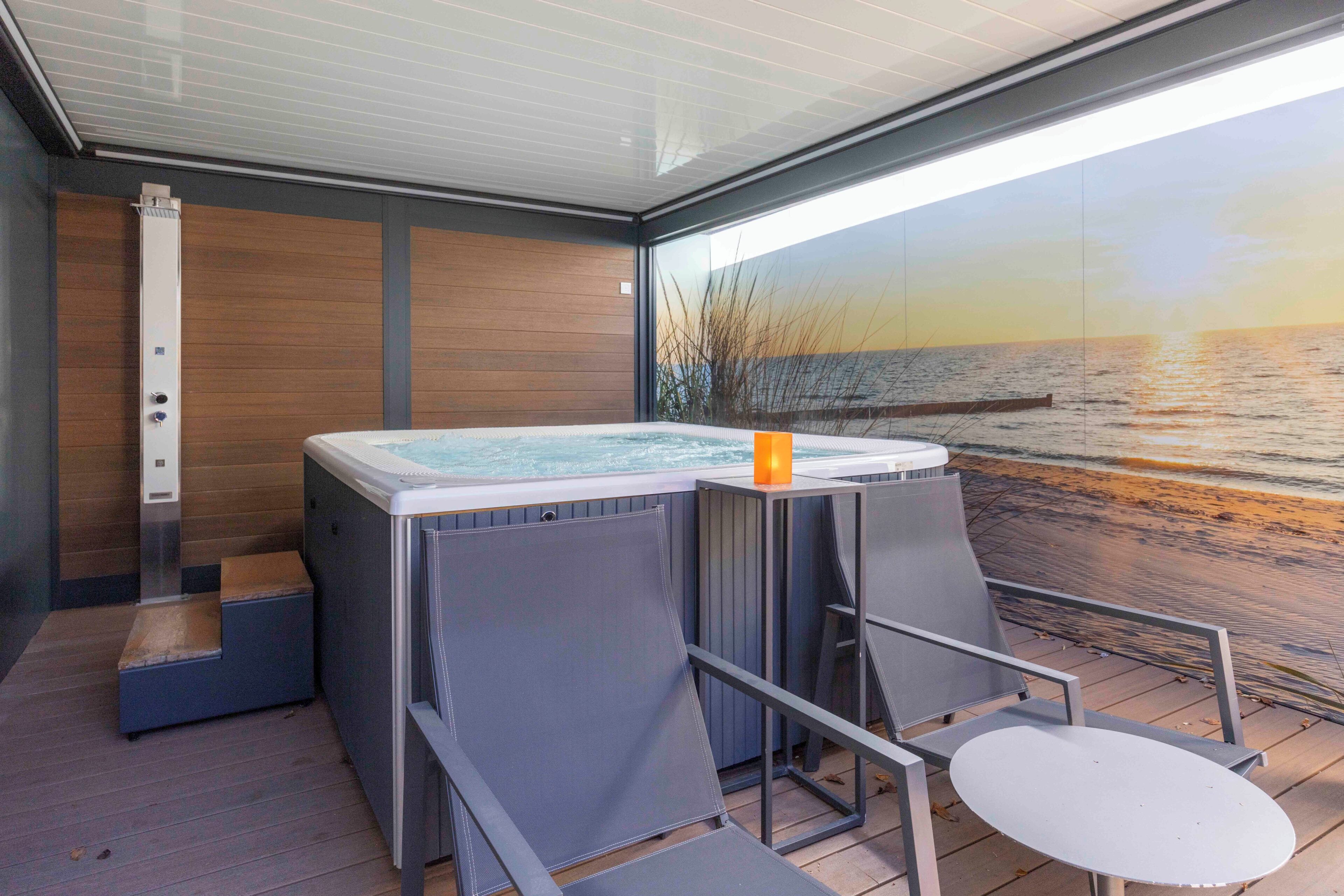A hot tub with a view of the sea, a small table, and a chair on a wooden deck.