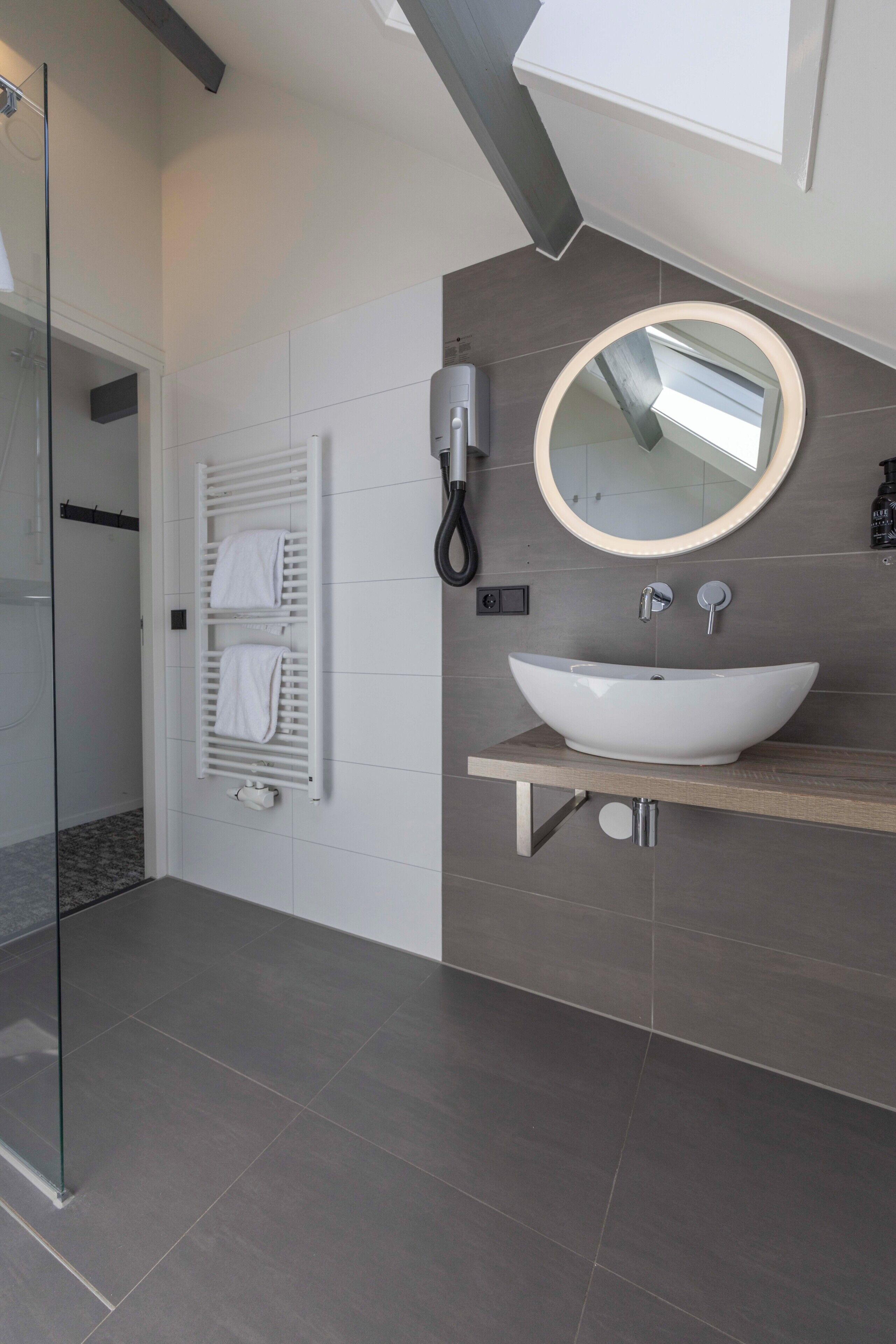 A modern bathroom with a glass shower, a white sink, a round mirror, and a towel rack.