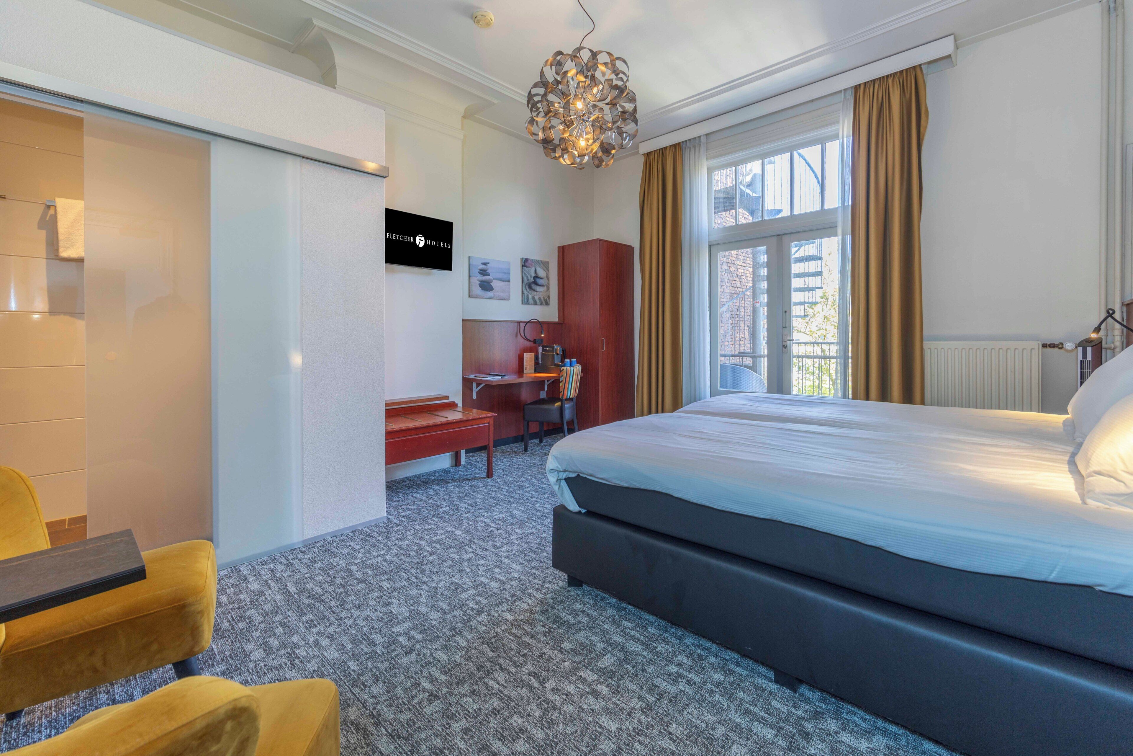 A hotel room with a large bed, a desk, a chair, and a wardrobe.