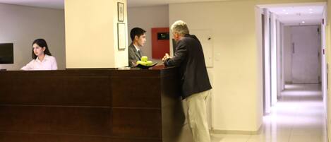 Mostrador de recepción con una recepcionista y dos huéspedes conversando.
