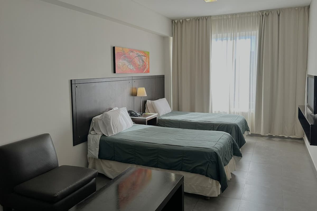 A hotel room with two beds, a desk, a chair, a TV, and a painting on the wall.