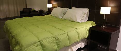 Una habitación de hotel con una cama grande, dos mesitas de noche con lámparas, una silla y un aparador.