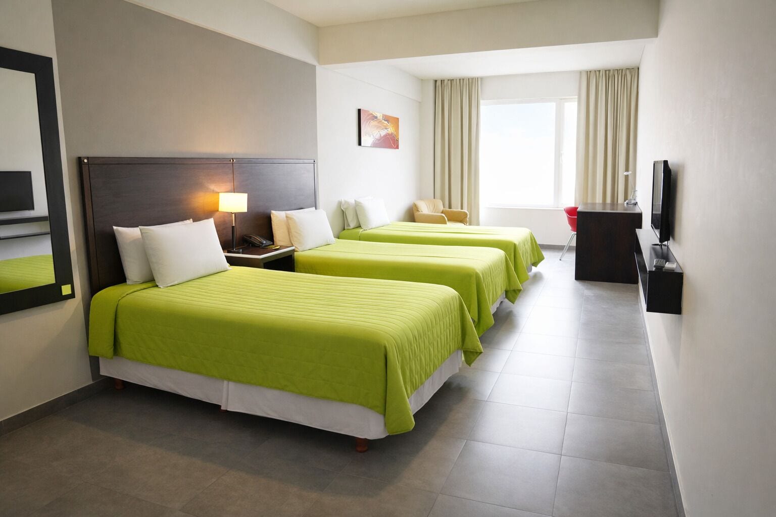 A hotel room with two beds, a desk, a chair, a television, and a window with curtains.