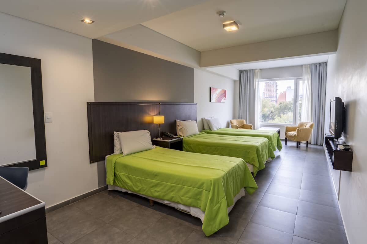 A hotel room with two beds, a desk, a chair, a TV, and a window with curtains.