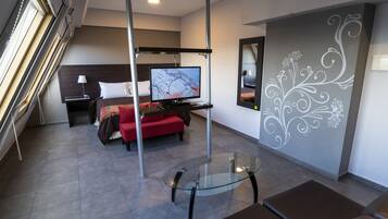 A modern hotel room with a bed, a TV on a stand, a glass table, and a decorative wall.