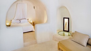 A modern bedroom with a bed, bedside table, and a glass table with a picture frame. - Azalea Houses (Santorini)