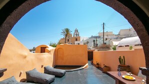 A rooftop terrace with a view of a village, including a church and palm trees. - Azalea Houses (Santorini)