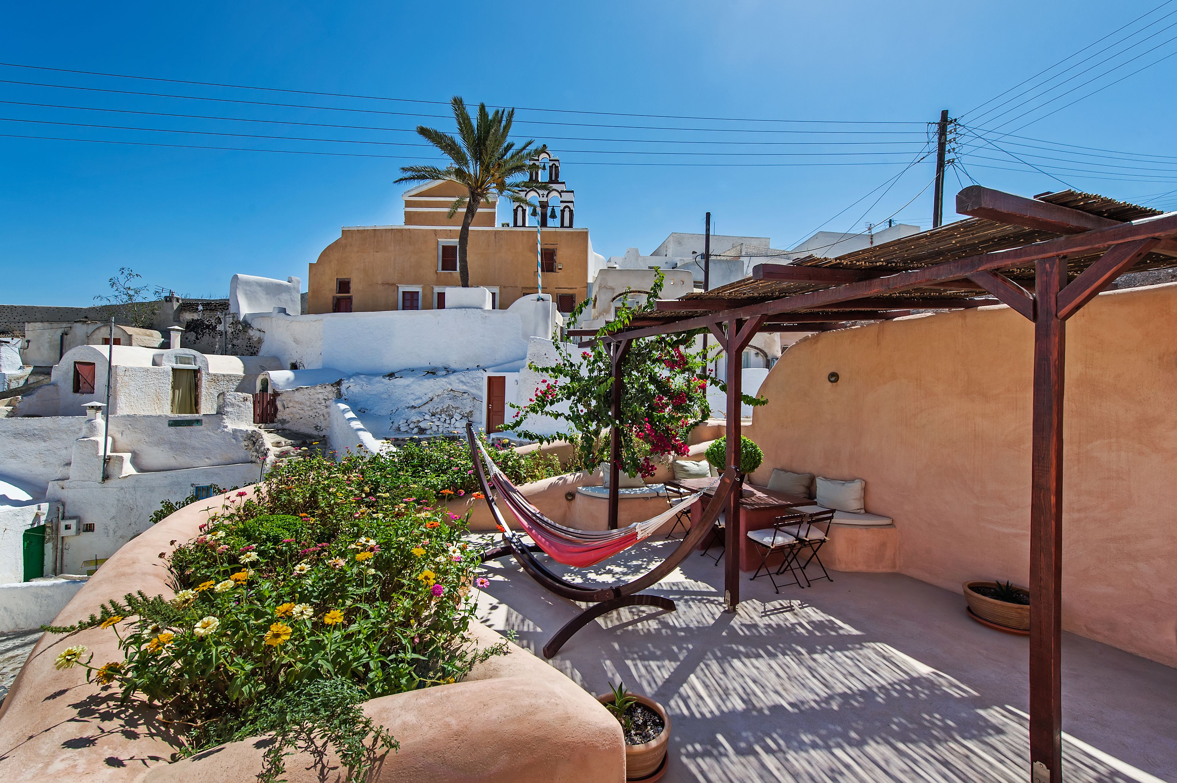 A rooftop terrace with a hammock, potted plants, and a view of traditional buildings.