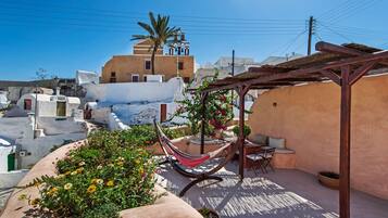 A rooftop terrace with a hammock, potted plants, and a view of traditional buildings.