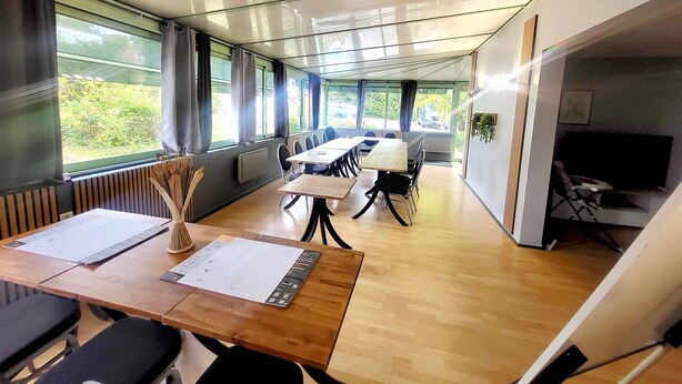 Een moderne vergaderruimte met houten tafels en stoelen, grote ramen en uitzicht op groen.