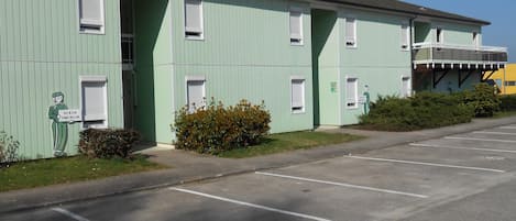 Un edificio verde con muchas ventanas y un estacionamiento al frente.