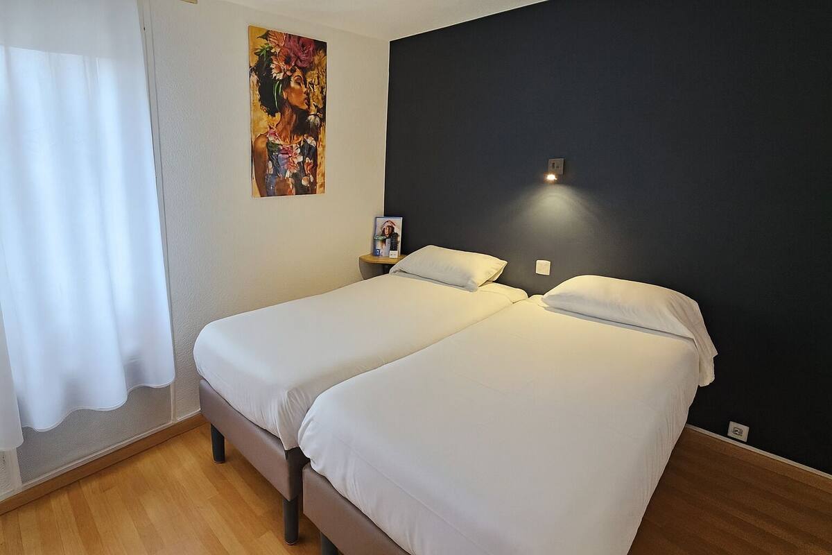 Habitación doble con una pared oscura, un cuadro y una mesita de noche con lámpara.