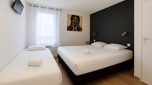 Een hotelkamer met twee bedden, een flatscreen televisie aan de muur, een schilderij en een deur met een handgreep.