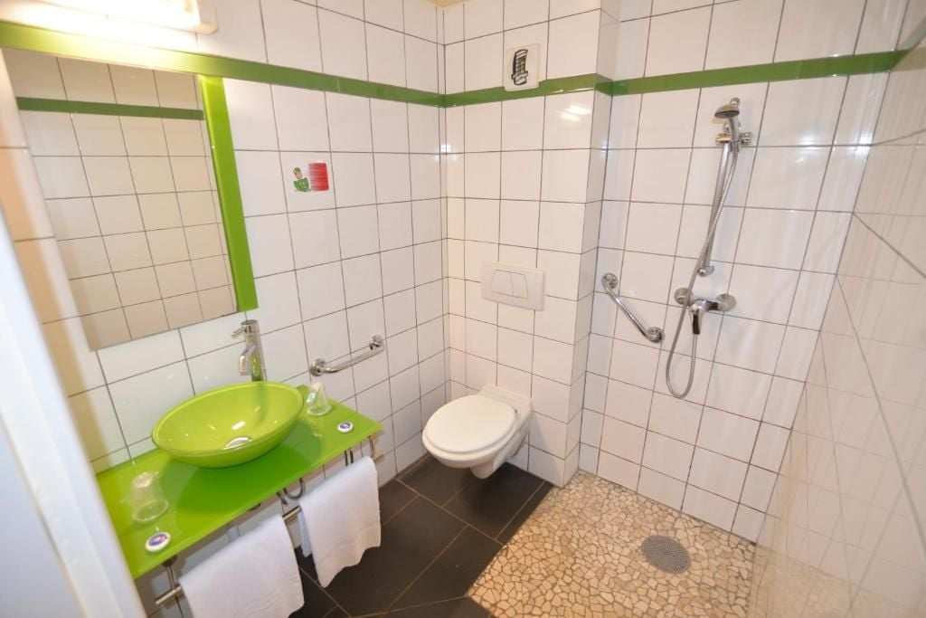 A bathroom with a green sink, white toilet, and a shower area.