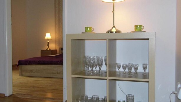 Una habitació amb llit, una nit i una taula de nit amb làmpada, i un armari de vidre amb diverses prestatgeries.
