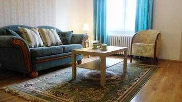 Uma sala de estar com um sofá azul, uma mesa de centro de madeira, um tapete estampado e uma cadeira.