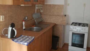 Una cuina petita amb armaris de fusta, un rentaplat i una estufa, i una làmpada penjant.