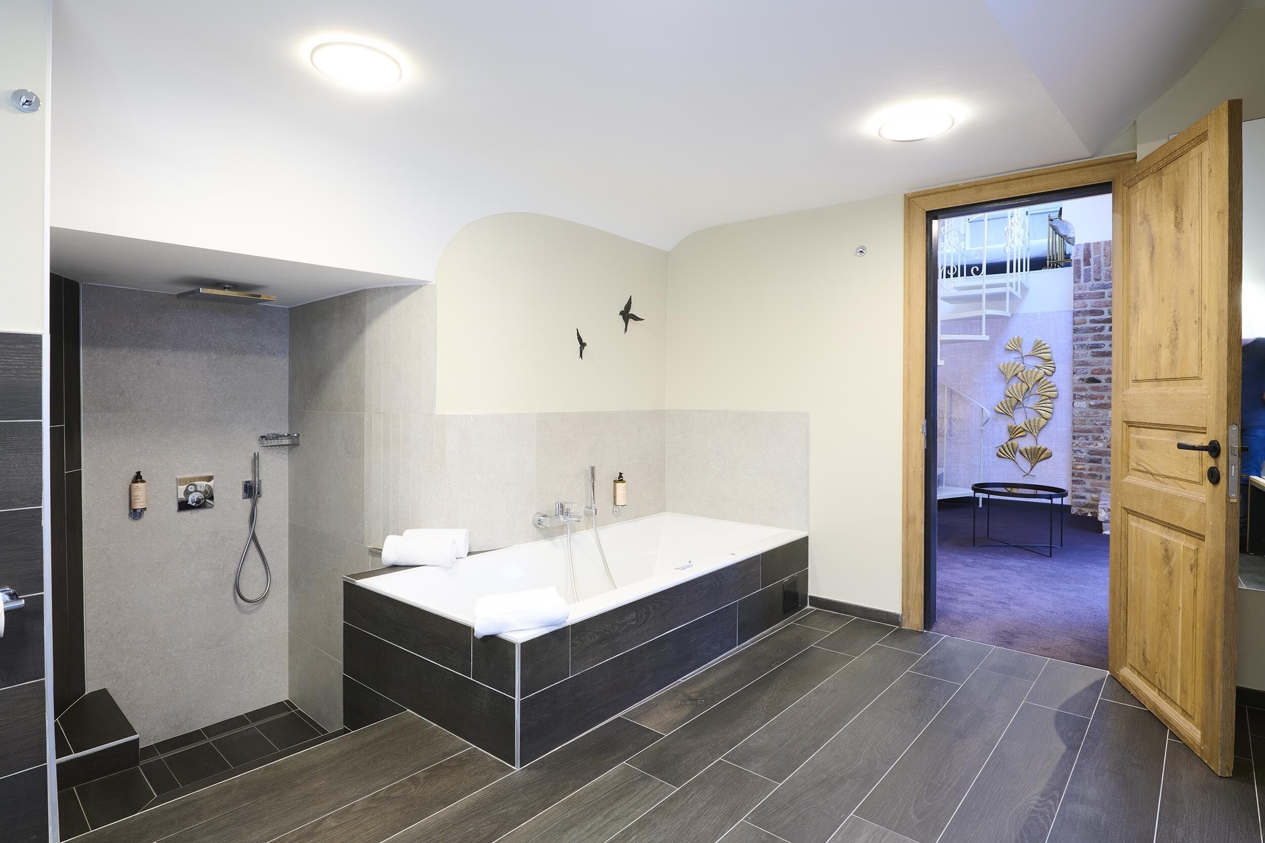 Een moderne badkamer met een ruim bad, een douchegedeelte en een houten deur naar een andere kamer.