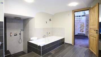 Een moderne badkamer met een ruim bad, een douchegedeelte en een houten deur naar een andere kamer.