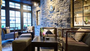 A cozy room with stone walls, a large window, and a comfortable seating area with a table and cushions. - Les Tanneurs de Namur (Namur)