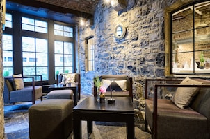 Una habitación acogedora con paredes de piedra, un ventanal grande y una zona de estar confortable con una mesa y cojines.