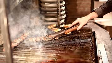 A person grilling meat on a grill with visible smoke.