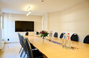 Une salle de conférence avec une longue table, des chaises, un écran de télévision et un vase rempli de fleurs.