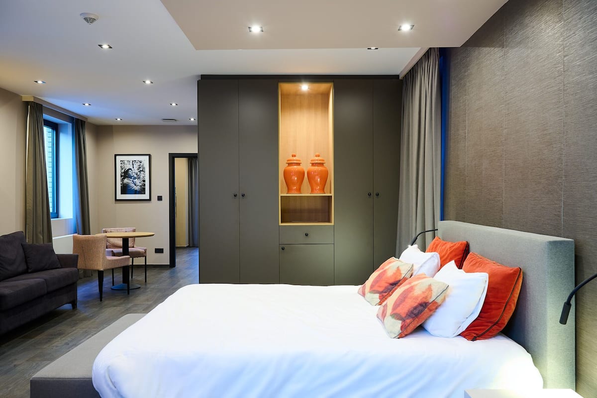 Una habitación de hotel moderna con una cama grande, un sofá, un comedor y un armario con estantes integrados.