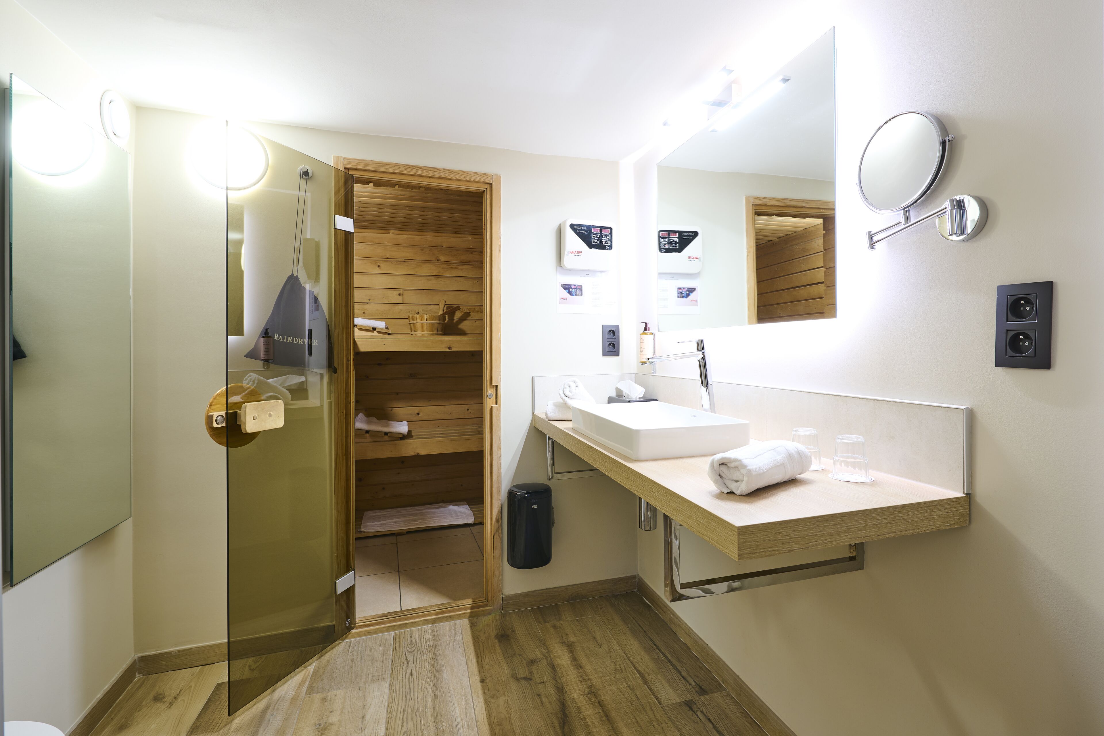 A modern bathroom with a glass shower enclosure, wooden shelving, a sink with a mirror, and a towel rack.