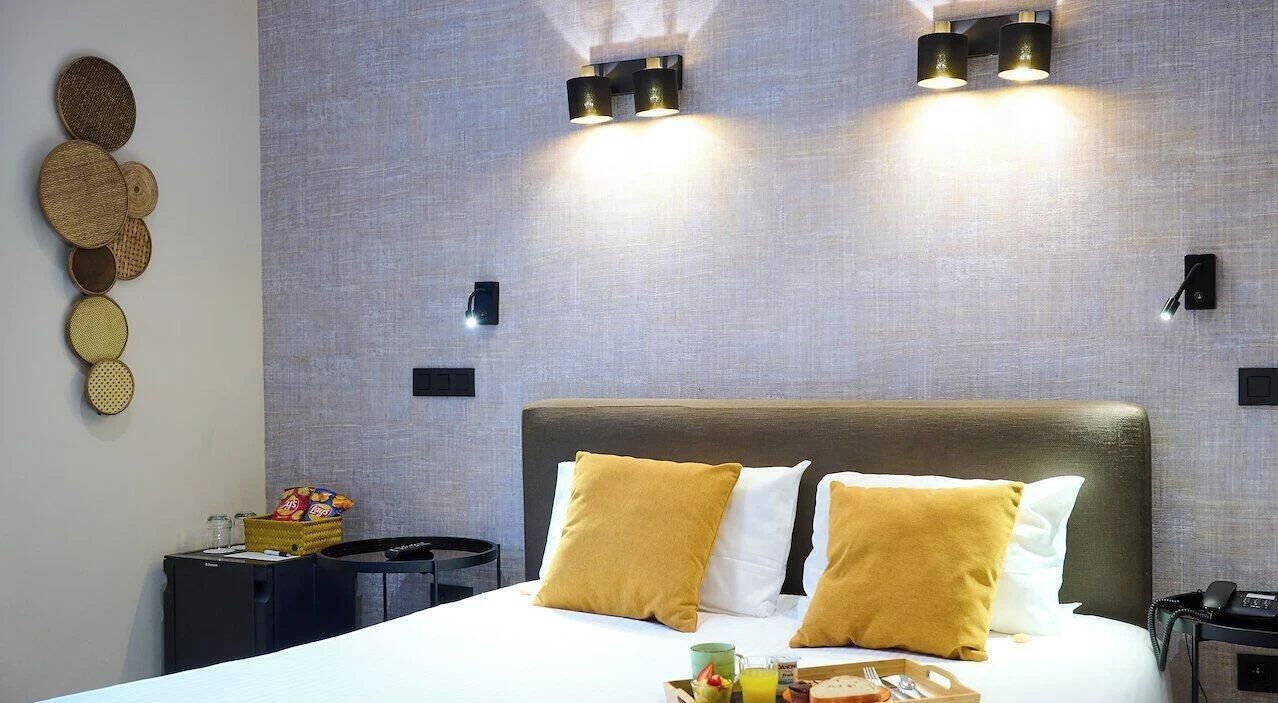 A hotel room with a large bed, two wall-mounted lights, a small side table, and a wall decoration.