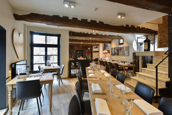 A restaurant with a long wooden table set for dining, a staircase, and a large window.