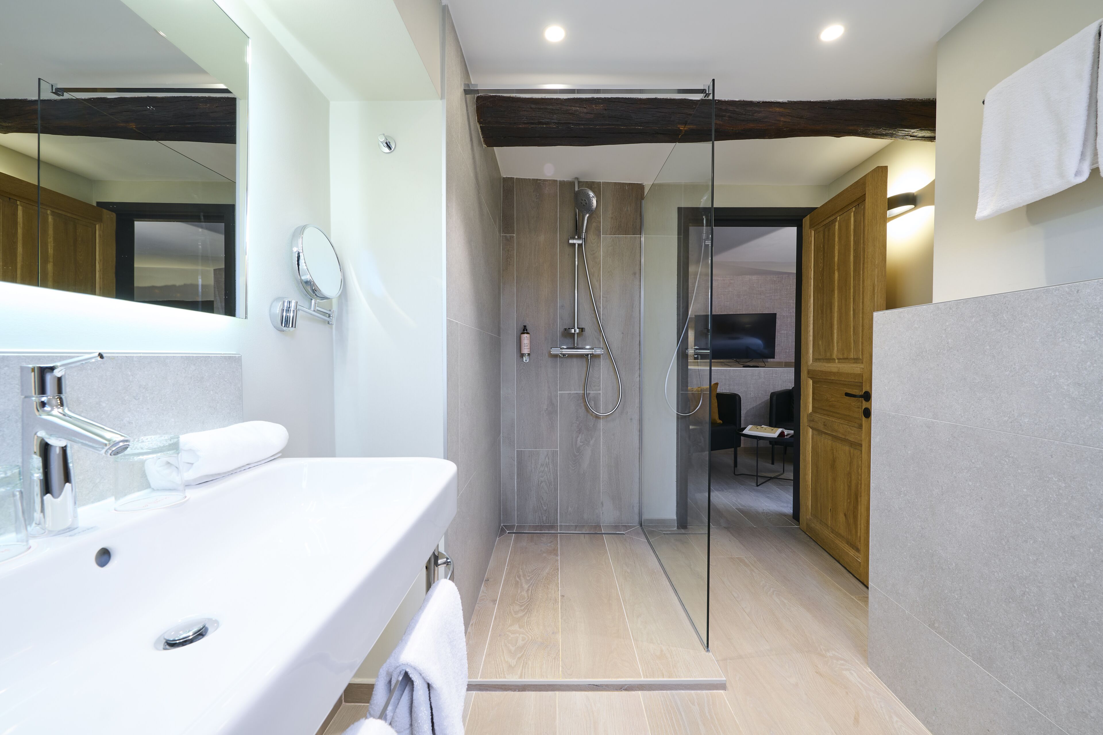 Un baño moderno con ducha de vidrio, un espejo grande y un lavabo blanco.