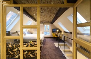 Un dormitorio con cama, escritorio y silla, una ventana y un techo con vigas a la vista.