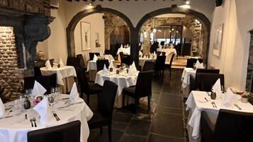Een restaurant met meerdere tafels klaar voor dineren, stenen muren en een metselwerk open haard.