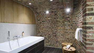 Une salle de bain moderne avec une grande baignoire, un meuble-lavabo en bois et un mur en briques.