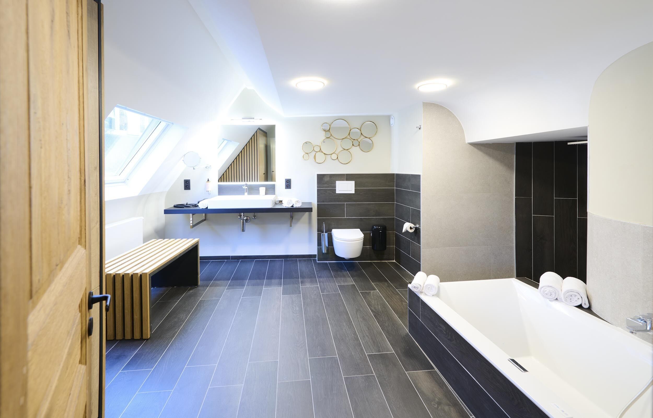 A modern bathroom with a skylight, a bathtub, a toilet, and a bench.
