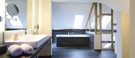 A modern bathroom with a large bathtub, a vanity with a mirror, and a skylight.