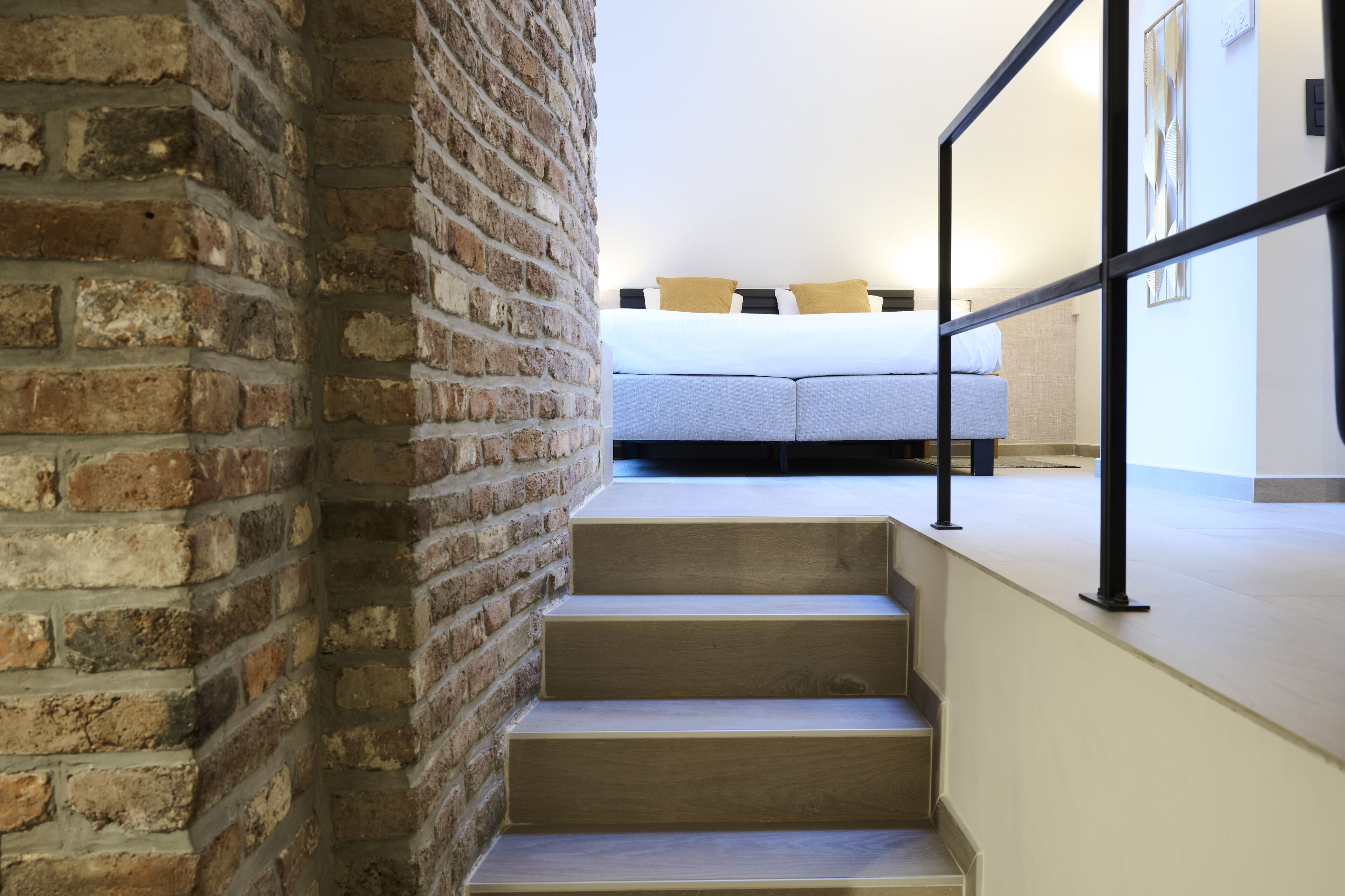 A staircase leading to a bed with a headboard, a brick wall, and a railing.