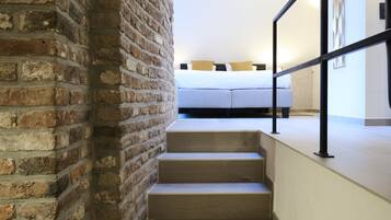 A staircase leading to a bed with a headboard, a brick wall, and a railing.