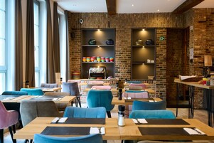 Un restaurant moderne avec des murs en briques, des chaises bleues et grises, des tables en bois et des étagères ornées d’objets décoratifs.