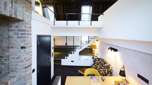 A modern interior with exposed brick walls, a staircase leading to a loft area, and a dining table with a lamp. - Les Tanneurs de Namur (Namur)