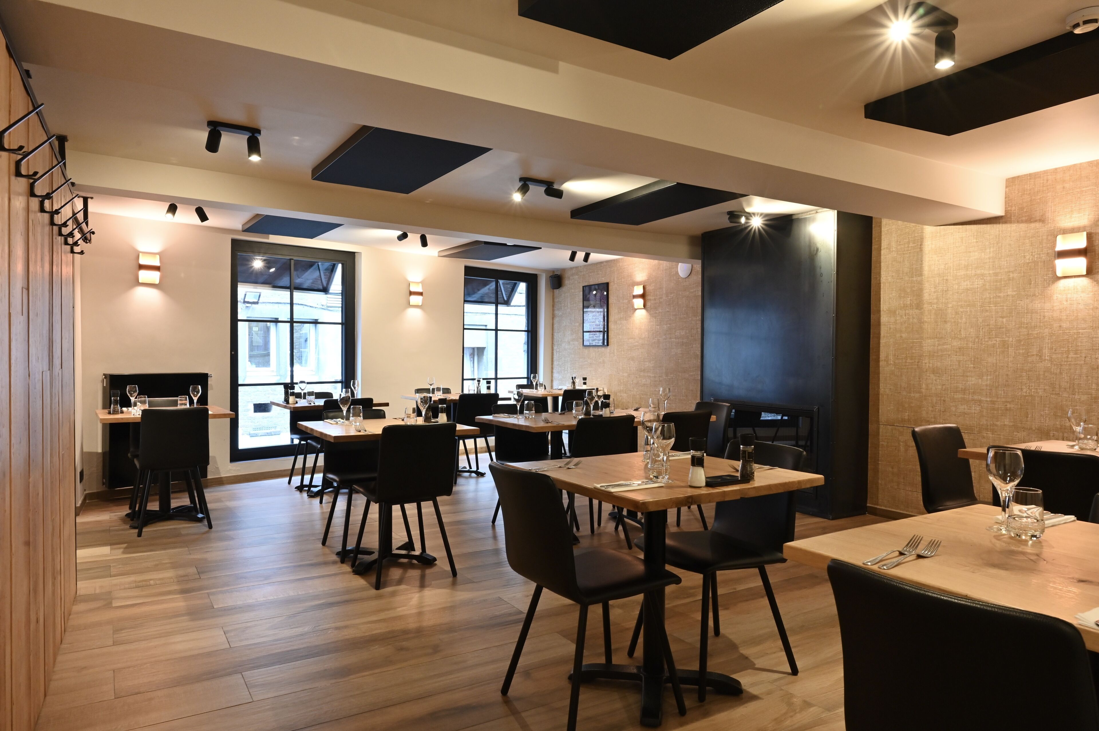 Un comedor moderno con varias mesas y sillas, suelo de madera e iluminación empotrada en el techo.