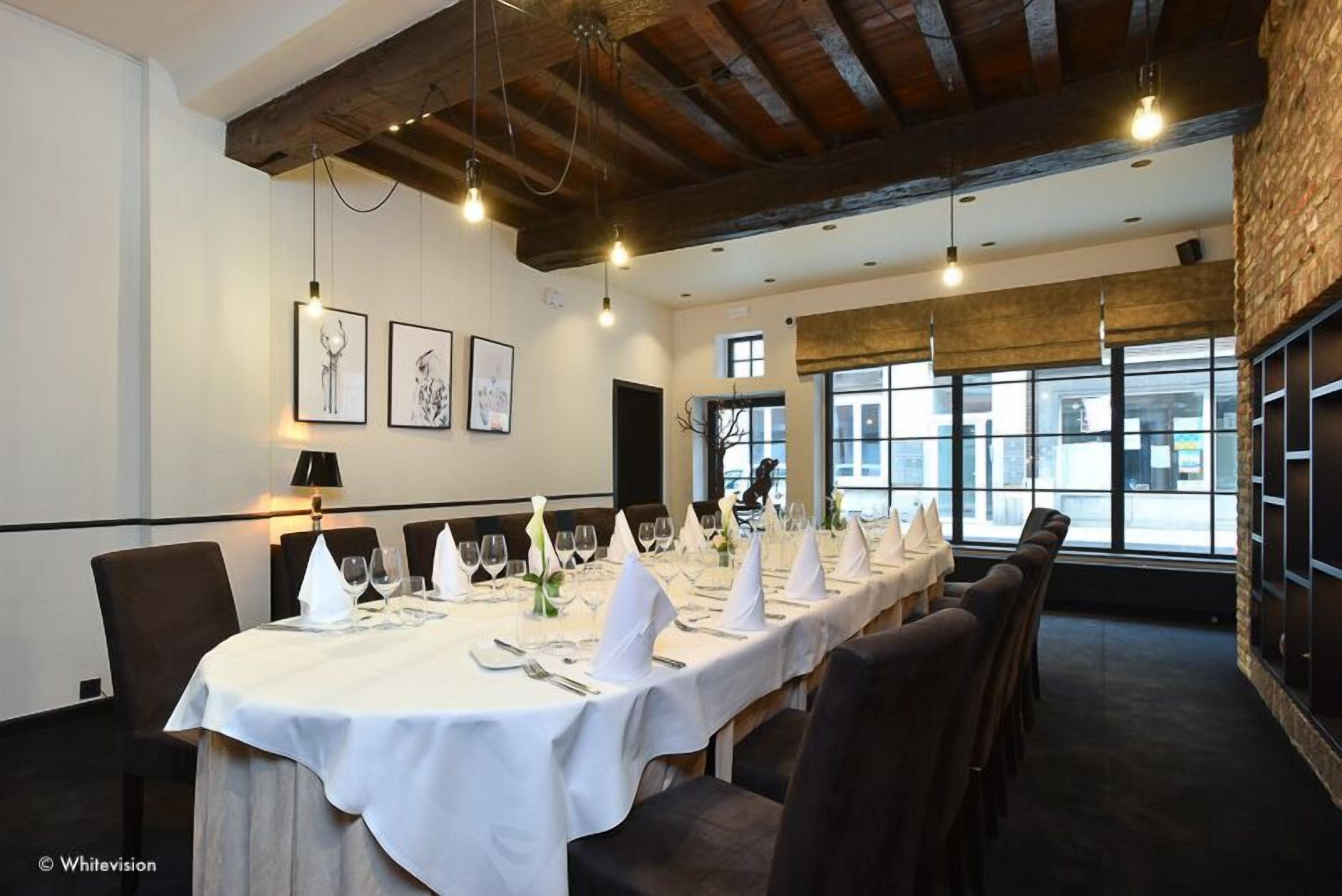 A dining area with a long table set for a meal, wooden beams on the ceiling, and framed artwork on the wall.