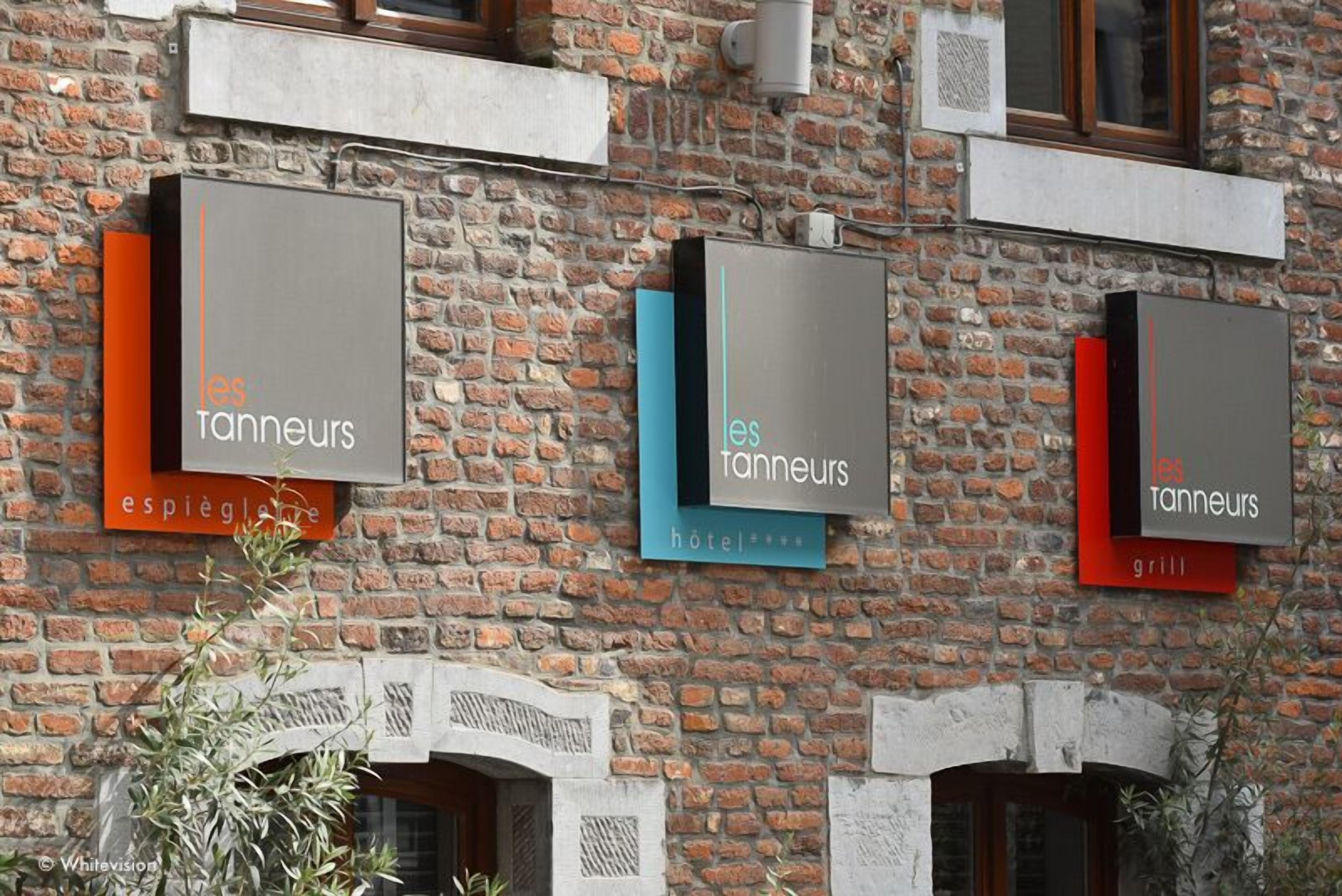 A building with three signs for 'les tanneurs' indicating different services: a restaurant, a hotel, and a grill.