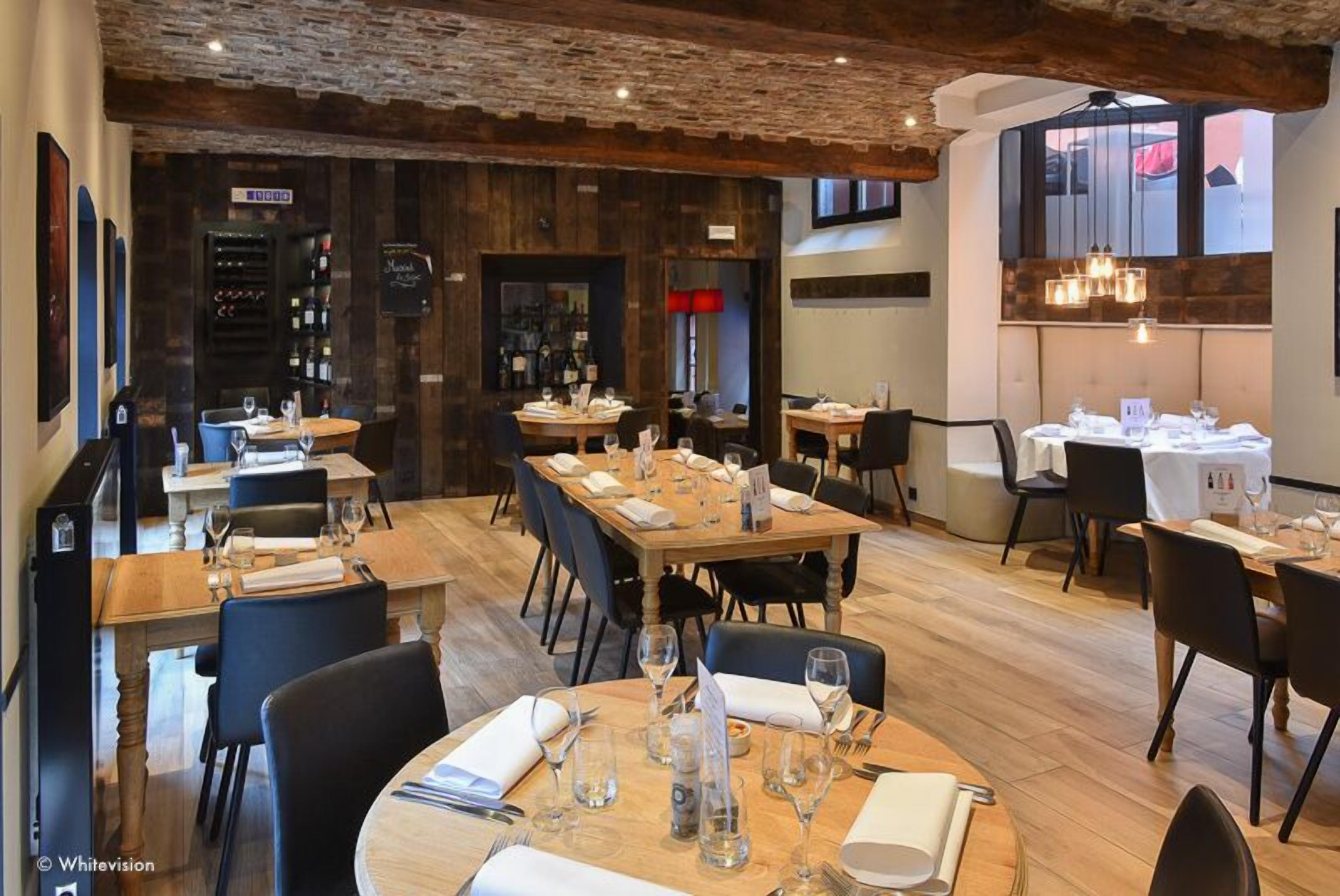 A restaurant with wooden tables and chairs, a brick ceiling, and a wine rack in the background.